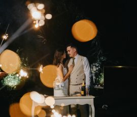 Noivos junto à mesa de bolo sob balões dourados enquanto fogo de artifício ilumina a noite, fotografia de casamento de Humberto Barbosa em Oliveira de Azeméis